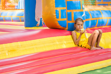 Image showing Girl sits at the entrance to an inflatable trampoline and eats an apple