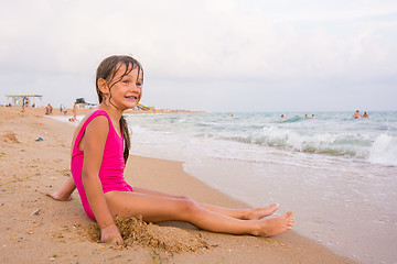 Image showing Five-year girl sits on a beach and seaside fun looking into the distance