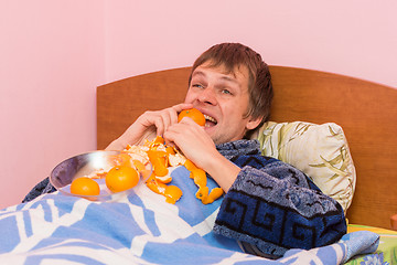 Image showing Happy young man biting tangerine lying in bed