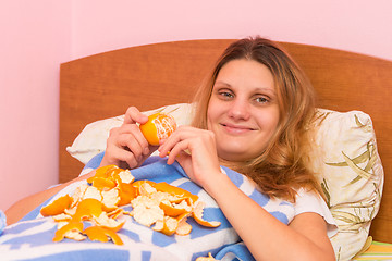 Image showing Cheerful girl eats tangerines lying in bed