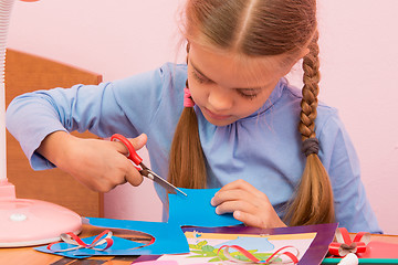 Image showing The child cuts off a piece of the blue colored cardboard