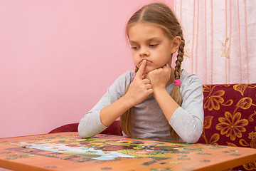 Image showing The child is thinking how to assemble a picture from puzzles