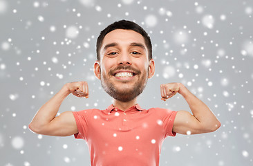 Image showing smiling man showing biceps over snow background