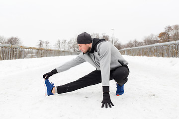 Image showing man exercising and stretching leg on winter bridge