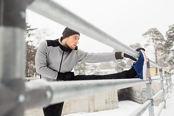 Image showing sports man stretching leg at fence in winter