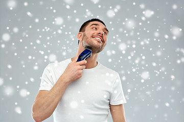 Image showing smiling man shaving beard with trimmer over snow