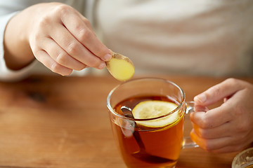 Image showing close up of woman adding ginger to tea with lemon