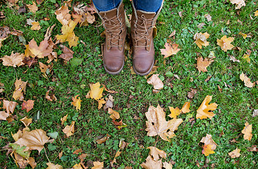 Image showing female feet in boots and autumn leaves on grass