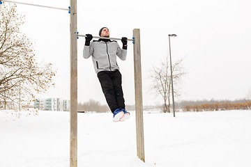 Image showing young man exercising on horizontal bar in winter