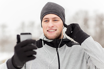 Image showing happy man with earphones and smartphone in winter