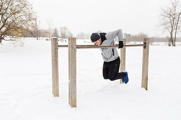 Image showing young man exercising on parallel bars in winter