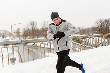 Image showing man with earphones running along winter bridge