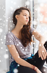 Image showing sad pretty teenage girl sitting on windowsill