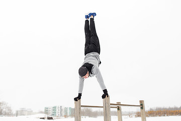 Image showing young man exercising on parallel bars in winter