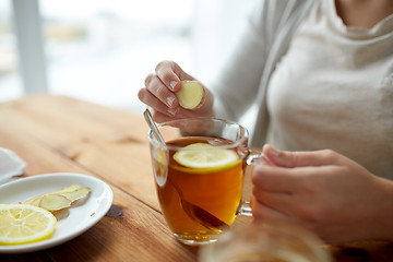 Image showing close up of woman adding ginger to tea with lemon