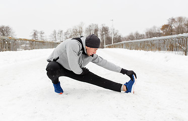 Image showing man exercising and stretching leg on winter bridge