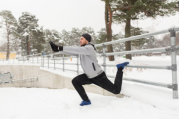 Image showing sports man stretching leg at fence in winter