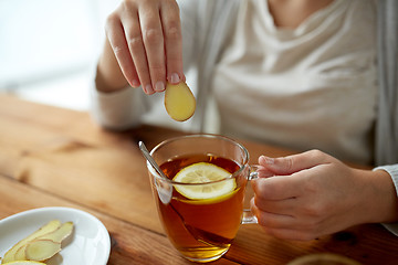 Image showing close up of woman adding ginger to tea with lemon