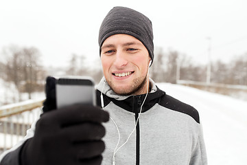 Image showing happy man with earphones and smartphone in winter