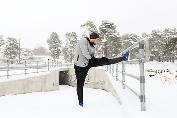 Image showing sports man stretching leg at fence in winter