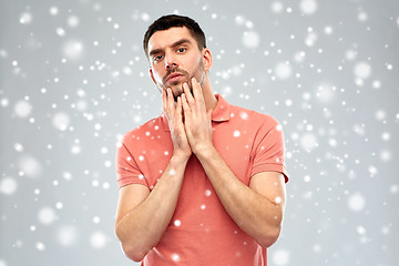 Image showing young man touching his face over snow background