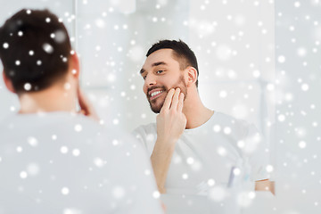 Image showing happy young man applying cream to face at bathroom