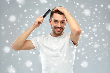 Image showing happy man brushing hair with comb over snow