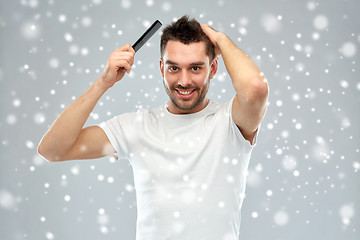 Image showing happy man brushing hair with comb over snow