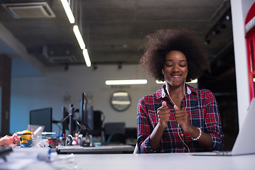 Image showing black woman in modern office speeking on phone over earphones