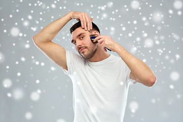 Image showing smiling man shaving beard with trimmer over snow