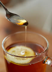 Image showing close up of woman adding honey to tea with lemon