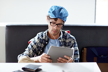 Image showing man with tablet pc and earphones sitting at cafe