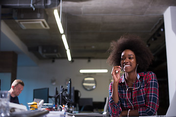 Image showing black woman in modern office speeking on phone over earphones