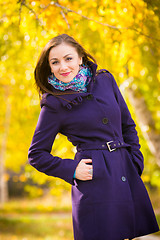 Image showing Self-confident girl in a dark blue coat against the background of autumn leaves