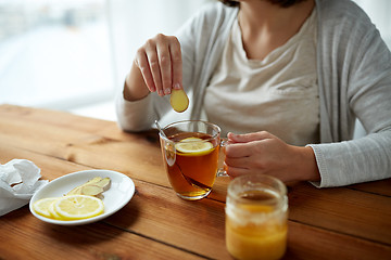 Image showing close up of woman adding ginger to tea with lemon