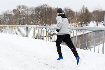 Image showing man in earphones running along winter bridge