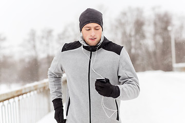 Image showing happy man with earphones and smartphone in winter