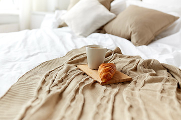 Image showing coffee cup and croissant on plaid in bed at home