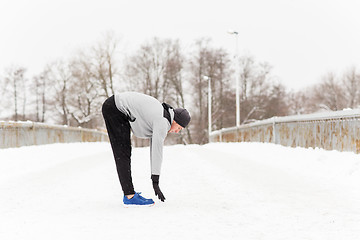 Image showing man exercising and stretching leg on winter bridge