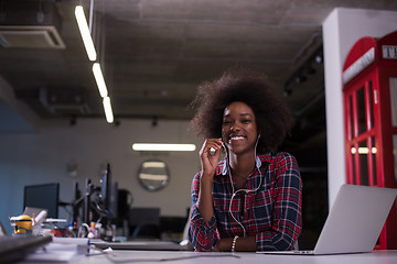 Image showing black woman in modern office speeking on phone over earphones