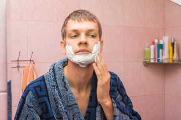 Image showing The young man gets shaving foam on his cheeks