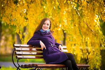 Image showing Young girl sitting on the bench warm autumn day