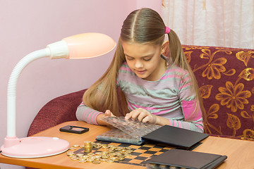 Image showing Girl at the table leafing through the album with coins