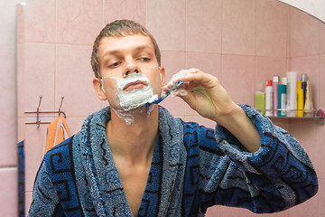 Image showing Young guy shaves neck in front of the mirror