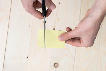 Image showing A man is cutting a sheet of yellow paper using metallic scissors