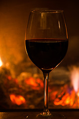 Image showing Glass of red wine in front of a fireplace