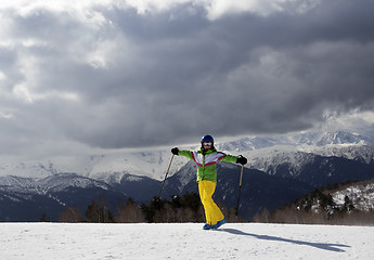 Image showing Happy young skier with ski poles in sun mountains and cloudy gra