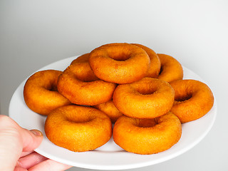 Image showing Male person holding a plate of freshly made dark brown doughnuts