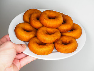 Image showing Male person holding a plate of freshly made dark brown doughnuts