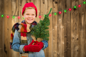 Image showing Happy Boy Wearing Santa Hat Holding Christmas Tree On A Wood Fen